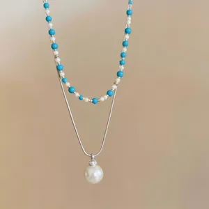 Dettaglio di una collana a due strati con perline blu e un pendente di perla bianca.