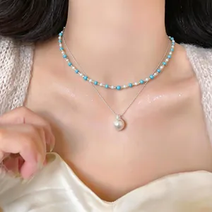 Dettaglio di una collana a doppio strato con perline turchesi e un grande ciondolo di perla