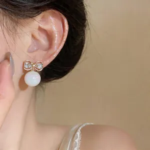 Close-up of bow stud earring with crystal inlay and iridescent pearl drop on model