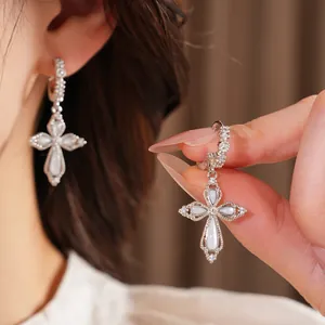 Vue macro détaillée d'élégantes boucles d'oreilles croix en zircon argenté avec fleurs.