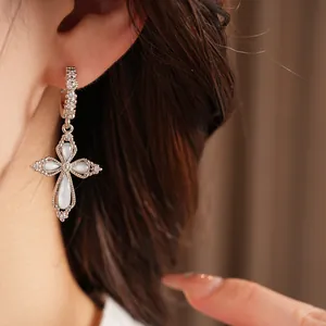 Détail d'une boucle d'oreille fleur en croix en zircon avec pierres opalescentes sur l'oreille du modèle