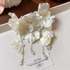 Detailed view of white fabric flower earrings with gold tassels and delicate pearls.