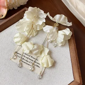 Macro view of elegant white fabric flower earrings featuring gold tassels and pearls