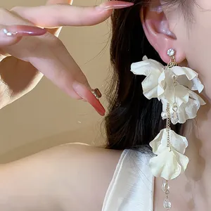 Detailed shot of white fabric flower tassel earrings with pearls on model's ear