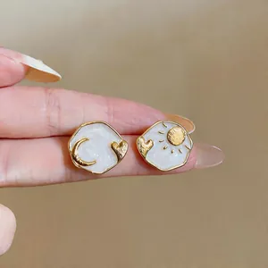 Close-up of asymmetric enamel heart earrings featuring golden sun and moon designs