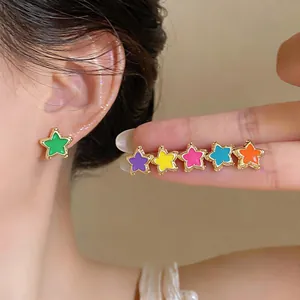 Detailed close-up showing vibrant colorful enamel star stud earrings worn on ear and hand