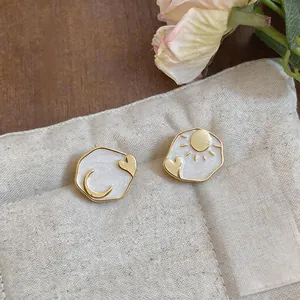 Close-up of asymmetric sun and moon enamel stud earrings on a linen texture background.