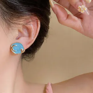 Detailed close-up of blue enamel earring with gold moon and heart patterns on ear