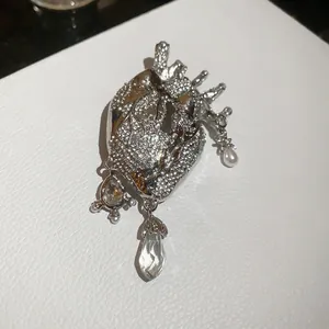 Macro detail of silver anatomical heart brooch with sparkling crystals and drop pendant