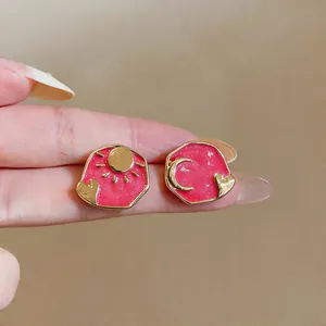 Macro close-up of pink enamel mismatched stud earrings with gold sun moon and heart designs