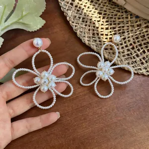 Primo piano di eleganti orecchini pendenti a forma di fiore di perle bianche traforate.