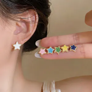 Detail of colorful star stud earrings in various enamel finishes on fingers and ear