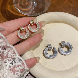 Close-up of gold and silver circular stud earrings with pavé and baguette zircon crystals