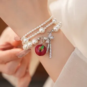 Elegante bracciale di perle multistrato con ciondolo a mela rossa e fiocco in zircone.