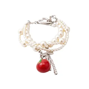 Elegante bracciale di perle multistrato con ciondoli a mela rossa e fiocco in zircone lucido.