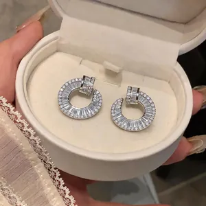 Macro detail of luxury silver-plated circular stud earrings with clear baguette zircons