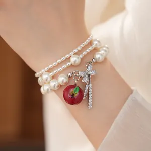 Elegante bracciale di perle a strati con ciondolo a mela e fiocco in zirconi.