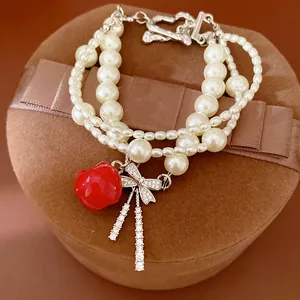 Dettaglio del bracciale di perle multistrato con mela rossa e ciondolo a fiocco