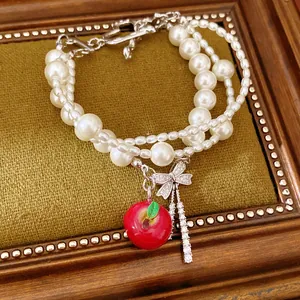 Dettaglio elegante di un bracciale di perle multistrato con ciondoli a mela e fiocco