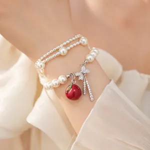 Dettaglio di bracciale di perle multistrato con fiocco in zircone e mela rossa