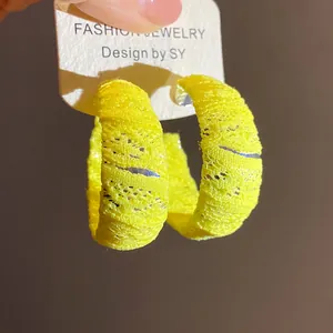 Dettaglio degli orecchini a cerchio a C avvolti in chiffon giallo su cartoncino