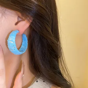 Dettaglio di orecchini a cerchio a forma di C avvolti in chiffon blu dallo stile sobrio.
