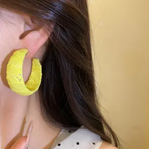 Primo piano di un orecchino a cerchio a C avvolto in chiffon giallo acceso sull'orecchio