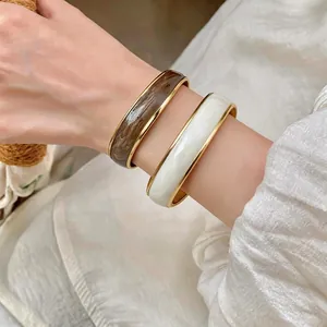 Eleganti bracciali aperti con strisce ondulate in marrone e bianco con bordo oro.