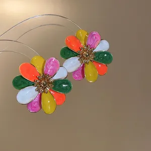Close-up detail of colorful enamel flower stud earrings featuring vibrant petals and gold centers