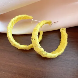 Dettaglio ravvicinato di orecchini a cerchio a C avvolti in chiffon giallo strutturato.