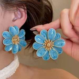 Detailed view of blue enamel flower stud earrings with golden textured centers on ear.