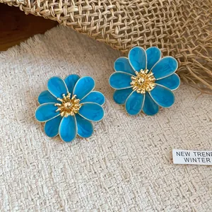 Close-up of blue enamel floral earrings with intricate gold centers on woven fabric