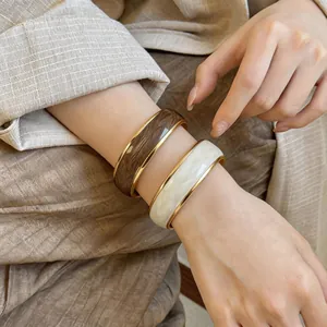 Vista dettagliata di bracciali in smalto marrone e crema con bordi dorati indossati sul polso.