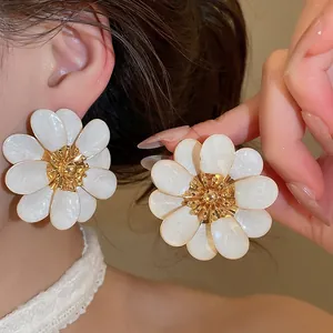 Detail close-up of large white oil-drip flower stud earrings with golden accents
