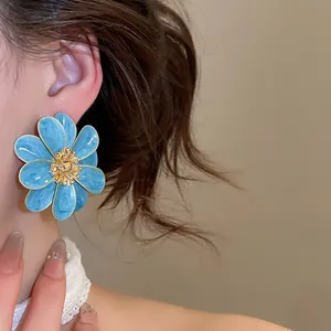 Detailed view of a blue enamel flower stud earring worn on a model's ear.