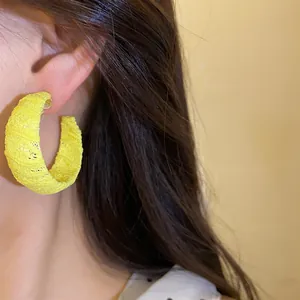 Primo piano dettagliato dell'orecchino a cerchio a C avvolto in chiffon giallo sul modello