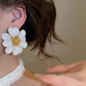 Detailed view of oversized white oil-drip flower earrings with gold center on model