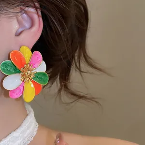 Detailed close-up of vibrant colorful enamel flower stud earring worn on model ear.