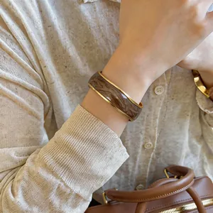 Elegante bracciale rigido dorato con un dettaglio unico marmorizzato marrone smaltato.