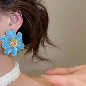 Close-up detailed view of light blue enamel flower stud earrings worn on a model's ear.