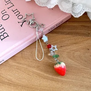 Close-up of sweet strawberry beaded phone strap with star clasp on pink book.