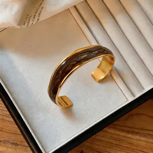 Dettaglio ravvicinato di un bracciale rigido dorato ondulato con smalto marrone