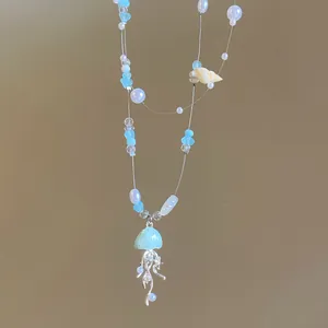 Primo piano di una collana di perle oceaniche con ciondolo a forma di medusa azzurra e conchiglie.