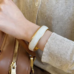 Elegante bracciale rigido dorato con smalto bianco a motivi a onde indossato al polso