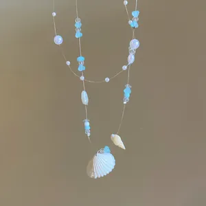 Dettaglio di una collana estiva in stile spiaggia con conchiglie e perline blu.