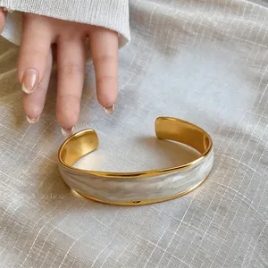 Dettaglio di bracciale rigido dorato con smalto marmorizzato a onde bianco e grigio