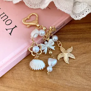 Close-up of a sweet gold keychain with white pearls, seashell, and starfish charms.
