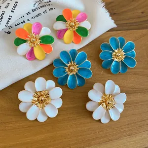 Close-up view of colorful and white enamel daisy flower earrings on a natural wood surface