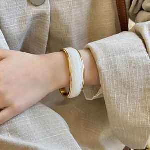 Primo piano dell'elegante trama in smalto bianco ondulato sul bracciale rigido dorato.