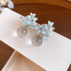 Close-up of light blue resin flower stud earrings with crystals and round beads.